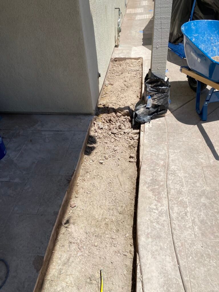 Deep utility trenching and concrete slab demolition for an emergency residential plumbing line repair near a house foundation and swimming pool using a mini excavator.