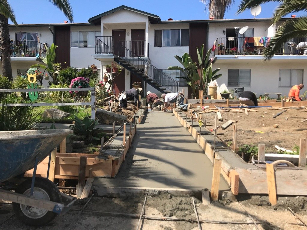 Commercial concrete installation at an apartment complex featuring newly formed and poured walkways and a structural masonry retaining wall after complete demo and removal by Cruz Construction & Development, Inc.